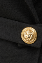 Close-up of a black garment with a gold button featuring a lion emblem.