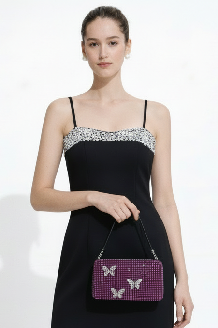 Woman holding a pink rhinestone handbag with butterfly designs against a white background