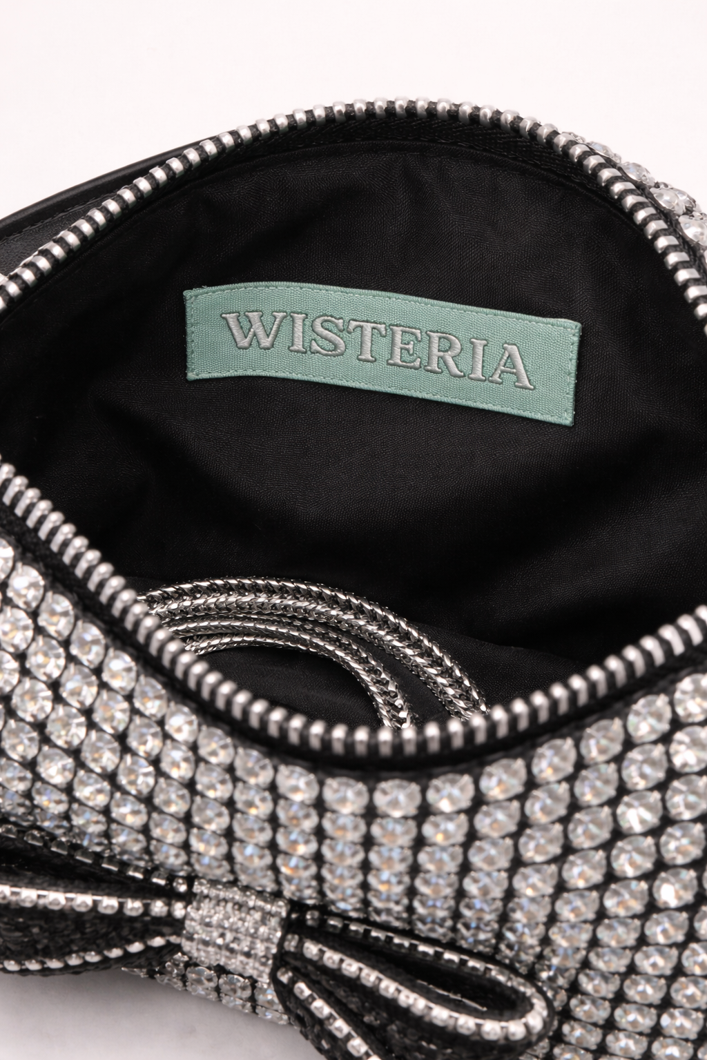 Close-up of a sparkling handbag with 'Wisteria' brand label on black interior. rhinestone bag